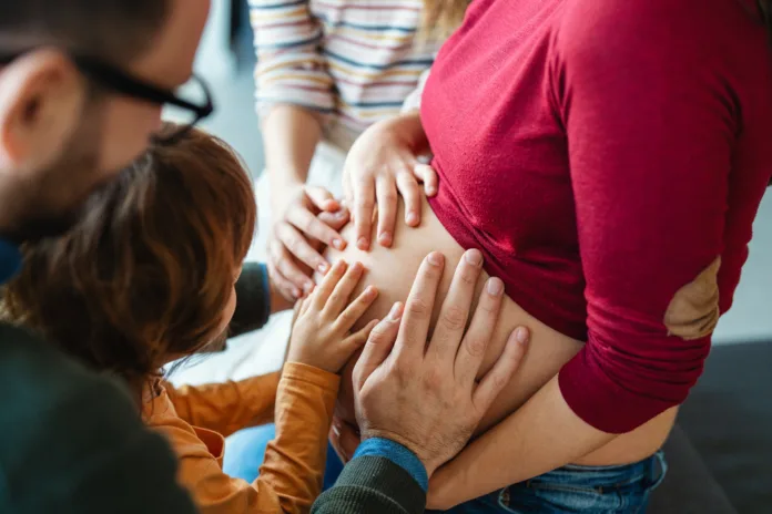 Família tocando a barriga de uma mulher grávida, simbolizando apoio e conexão durante a gestação. Imagem ilustrativa para matéria sobre licença-maternidade e licença-paternidade no serviço público.