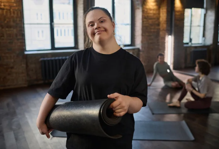 Jovem com Síndrome de Down segurando um tapete de yoga em ambiente de aula. Imagem ilustrativa para matéria sobre aprovação de política nacional para inclusão e direitos de pessoas com Síndrome de Down.