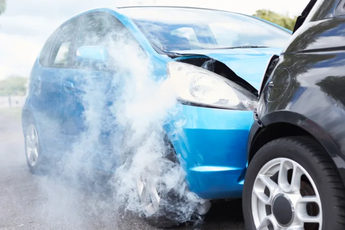 Imagem de um acidente de trânsito envolvendo dois veículos, com destaque para um carro azul com a frente danificada e fumaça saindo do motor. A cena ilustra a gravidade de colisões causadas por imprudência no trânsito, como excesso de velocidade ou negligência, abordados na matéria sobre o acidente na BR-116.