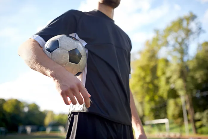 Jogador de futebol segurando uma bola no braço em campo ao ar livre. Imagem ilustrativa para matéria sobre direito de imagem e remuneração de atletas.