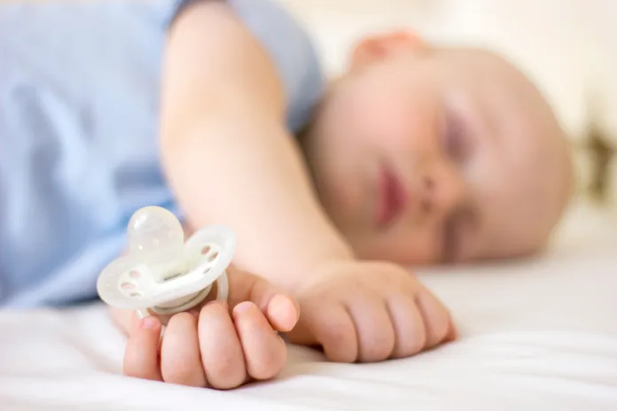 Bebê dormindo segurando uma chupeta branca, representando o tema da decisão do TST sobre a conduta inadequada de um enfermeiro na UTI.