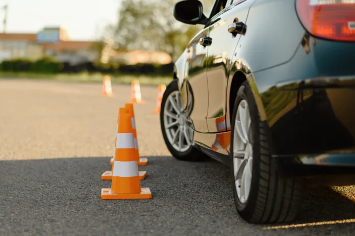 Carro de autoescola realizando manobra entre cones em pista de treinamento. Aulas práticas de direção são essenciais para a obtenção da CNH.