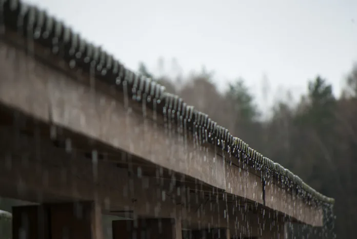 Chuva intensa escorrendo pelo telhado de uma estrutura de madeira, representando problemas de escoamento e drenagem urbana.