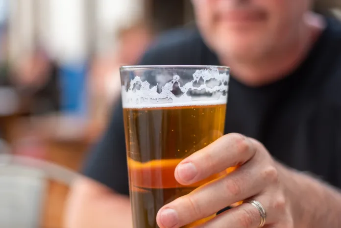 Homem segurando um copo de cerveja em ambiente externo, representando a proibição da venda de bebidas alcoólicas às margens de rodovias federais.