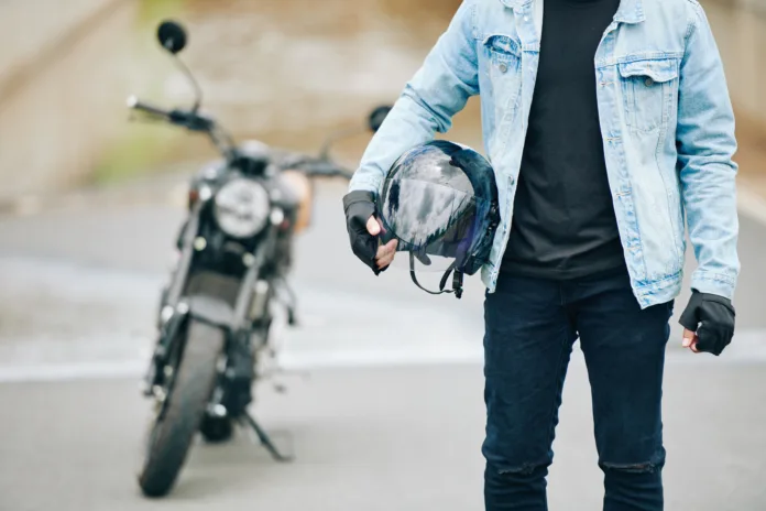 Motociclista segurando capacete ao lado de sua moto em via pública. Imagem ilustrativa para matéria sobre a decisão do TRT-MG que negou o adicional de periculosidade para motociclistas por falta de norma regulamentadora válida.