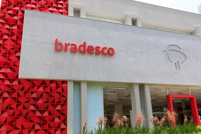 Fachada de agência do Banco Bradesco com logotipo vermelho. Imagem ilustrativa para matéria sobre condenação do banco pelo TST ao pagamento de horas extras por cursos obrigatórios fora do expediente.